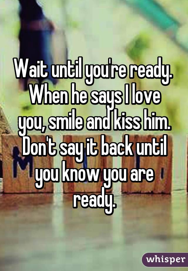 Wait until you're ready. 
When he says I love you, smile and kiss him. Don't say it back until you know you are ready.