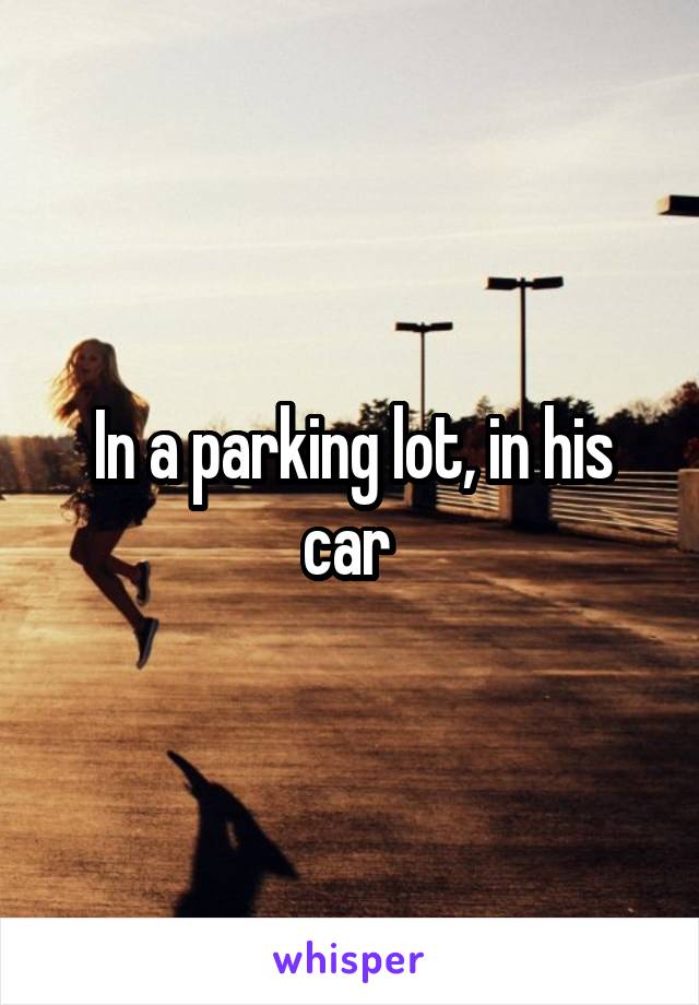In a parking lot, in his car 
