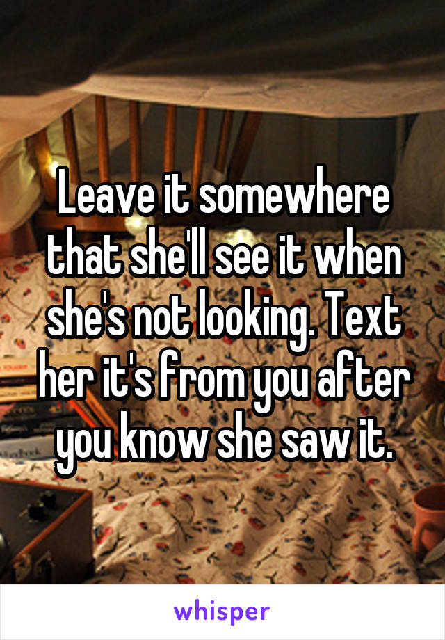 Leave it somewhere that she'll see it when she's not looking. Text her it's from you after you know she saw it.